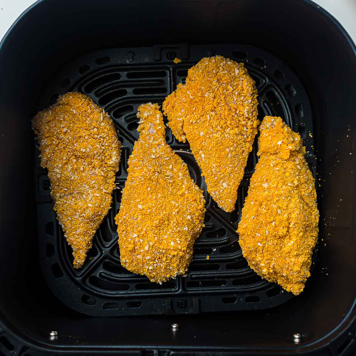 Breading chicken placed in air fryer basket.