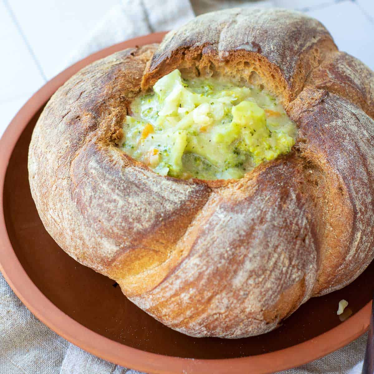 Broccoli cheddar soup bread bowl on a brown plate.