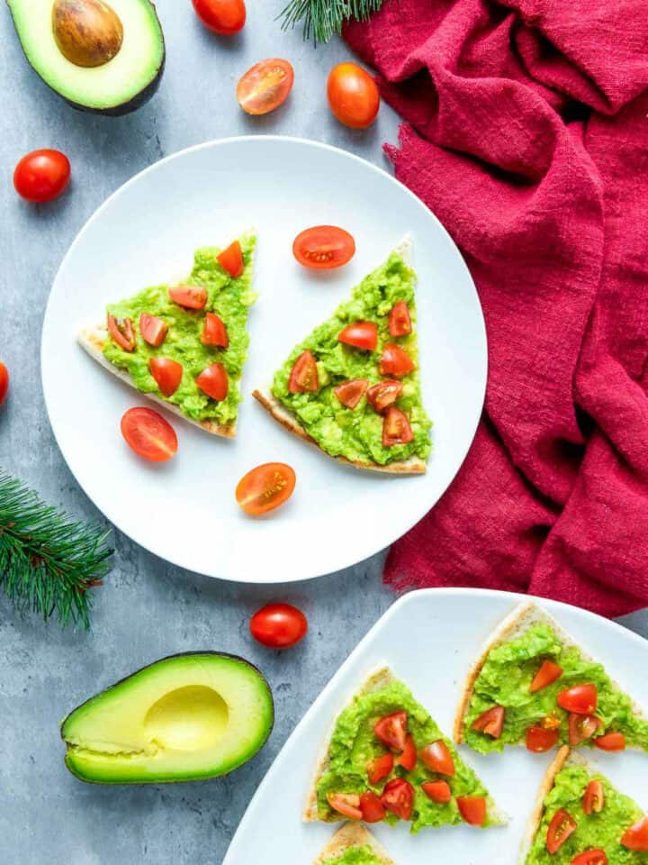 Two plates of Christmas appetizers with avocado in the background.