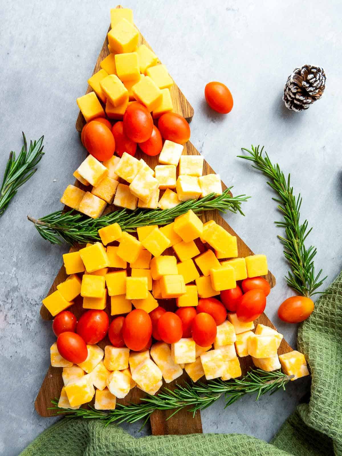 Christmas tree shaped cheese platter on a grey surface with rosemary in the background.