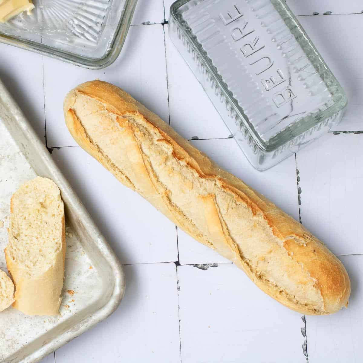 Whole and sliced baguette placed on white surface and baking sheet.