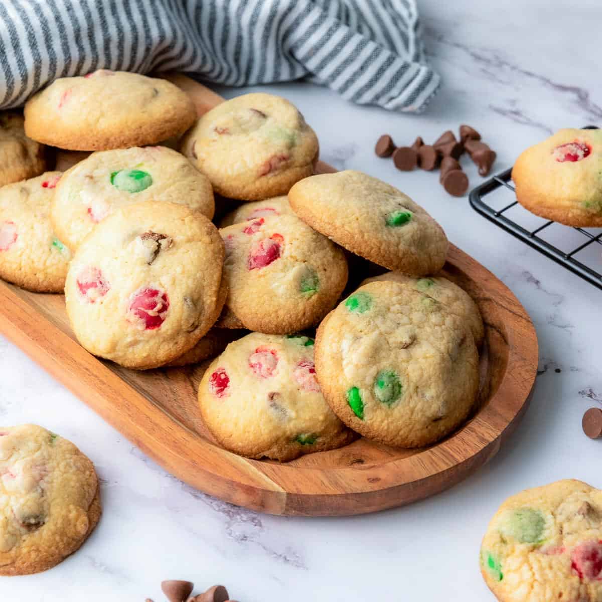 M&M cookies on a wooden board with chocolate chips in the background.