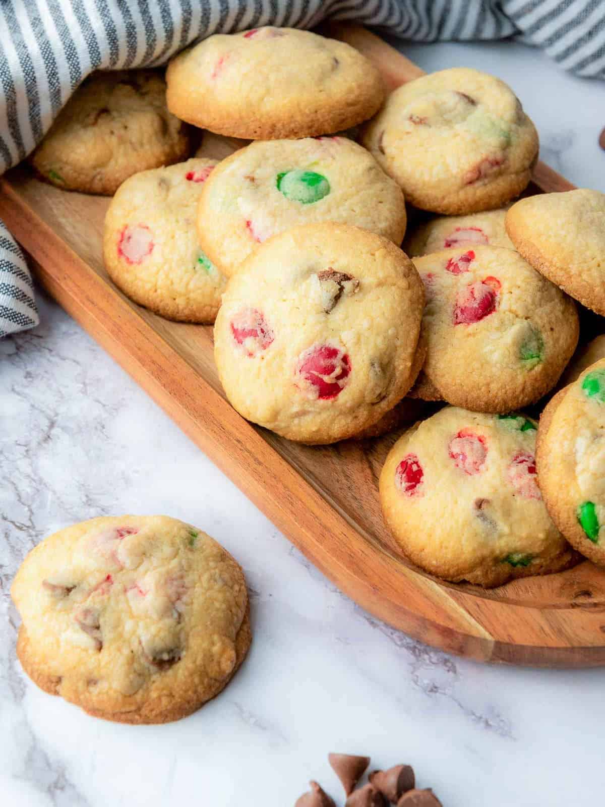 M&M cookies on a wooden plate placed on a a marble surface.