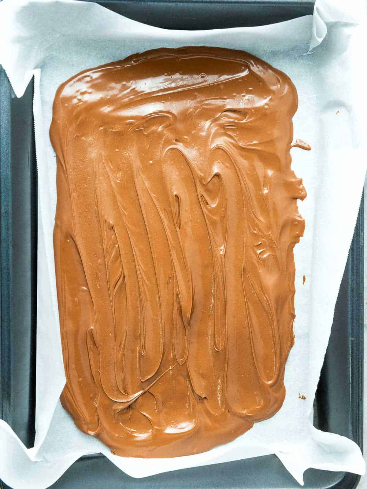 Melted chocolate spread on a lined baking tray.