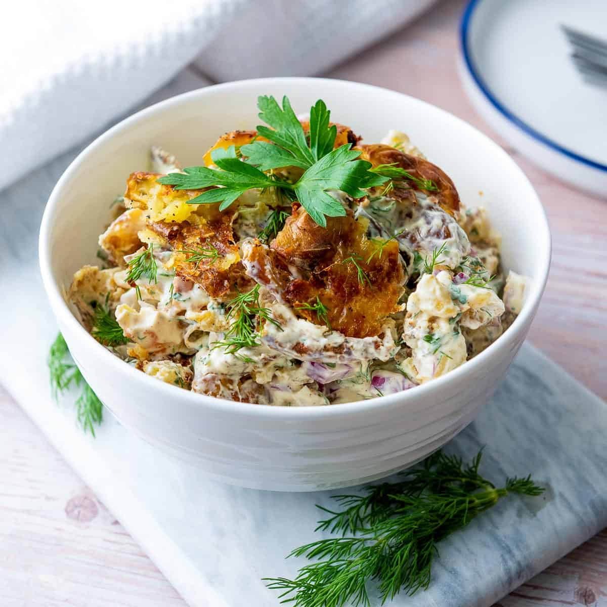 Smashed potato salad in a white bowl.