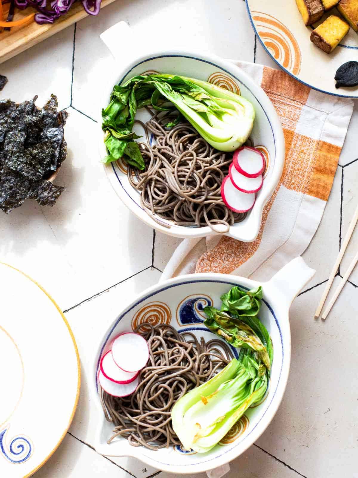 Assembling tofu bowls with noodles and sauted vegetables.