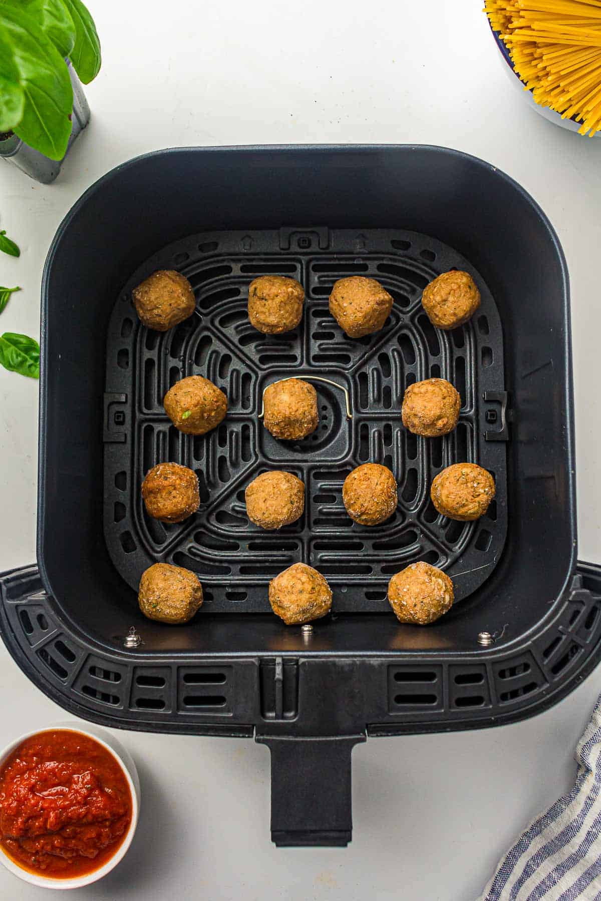 Frozen meatballs placed in air fryer basket.