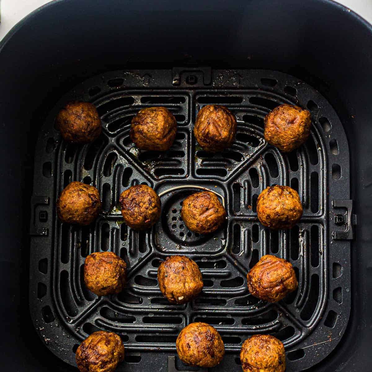 Cooked meatballs in air fryer basket.