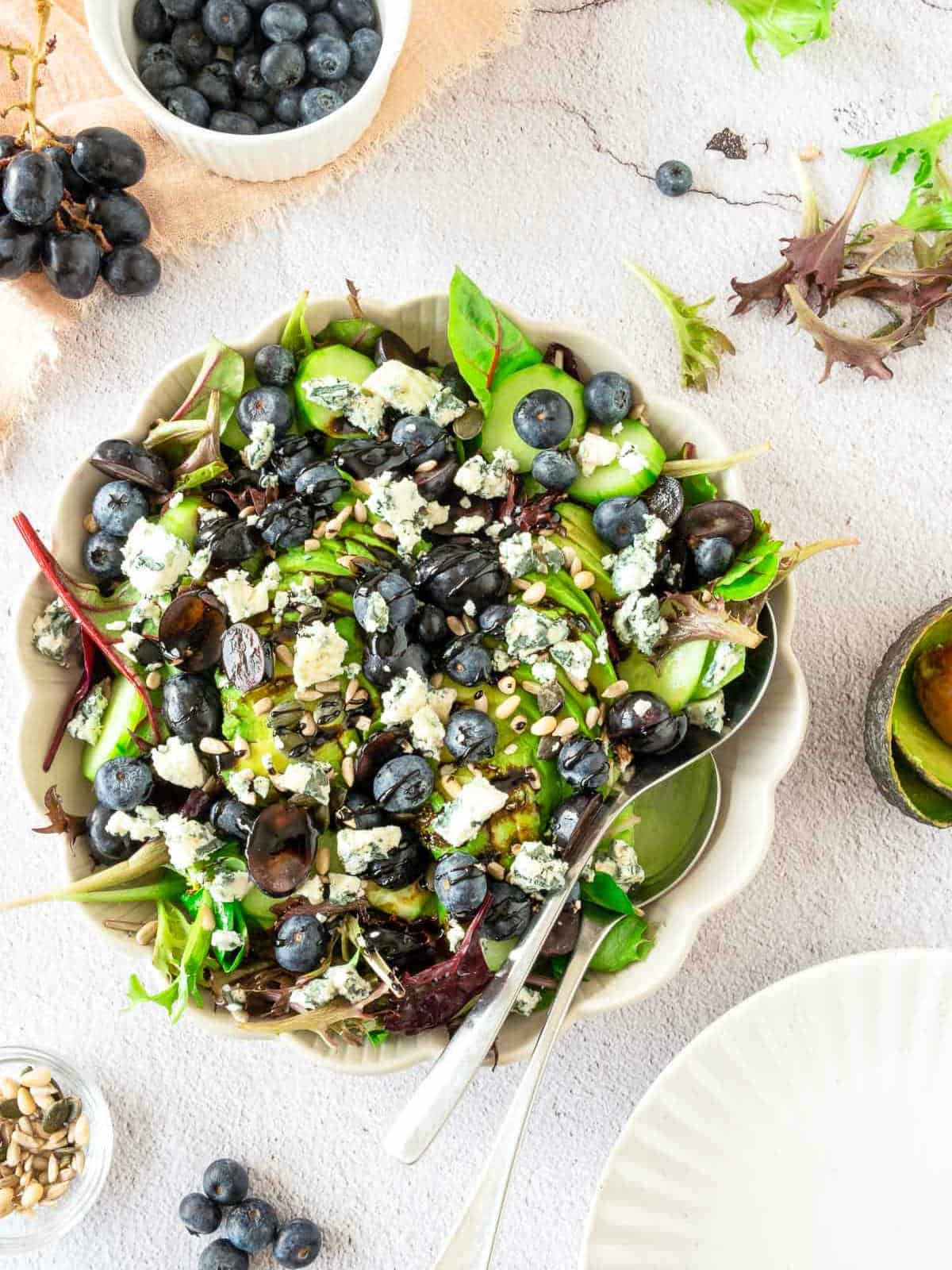 Blueberry grape salad in a white bowl with blueberries, grapes and seeds in the background.