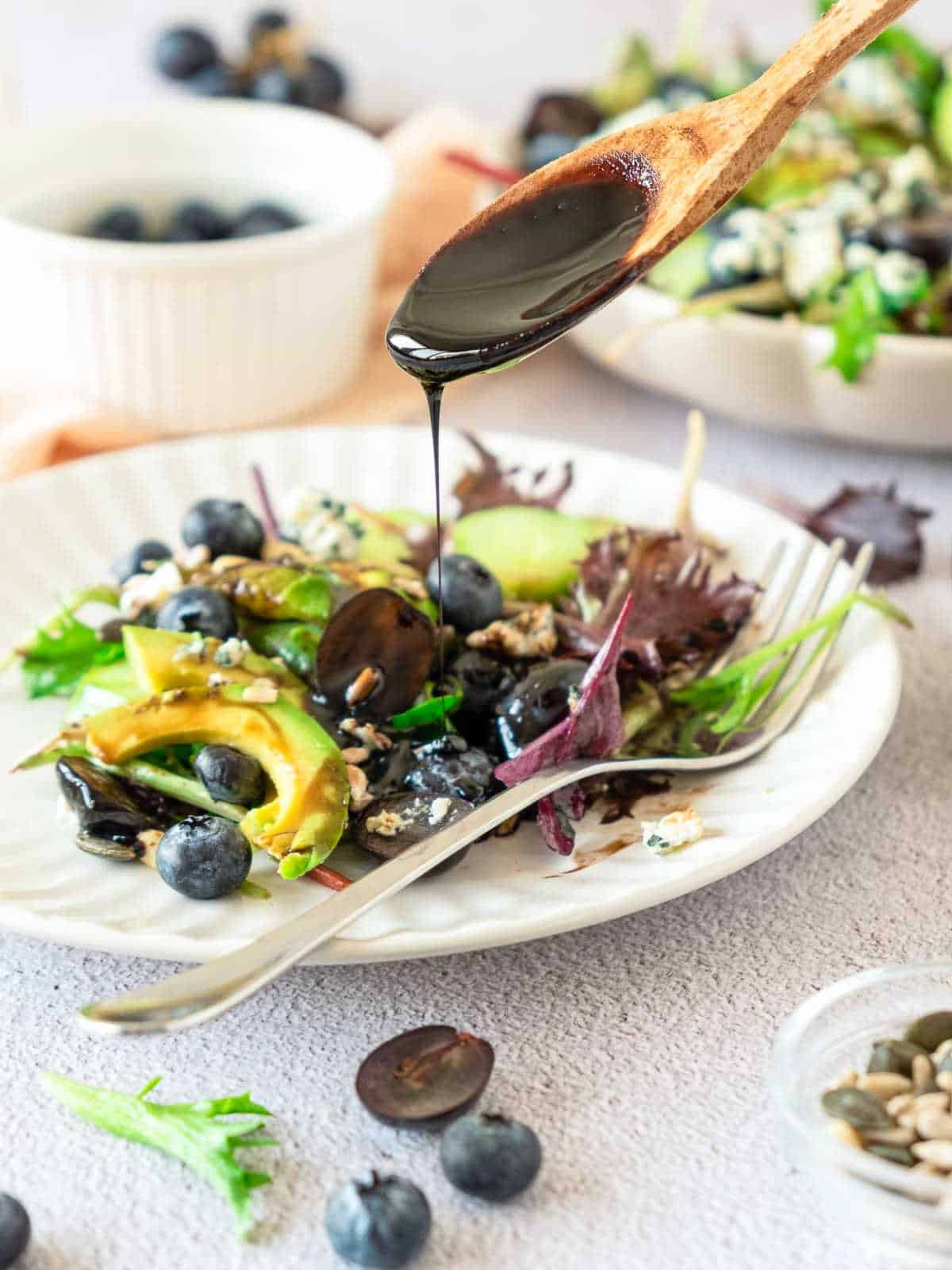 Pouring balsamic galze on individual salad servings on a white plate.