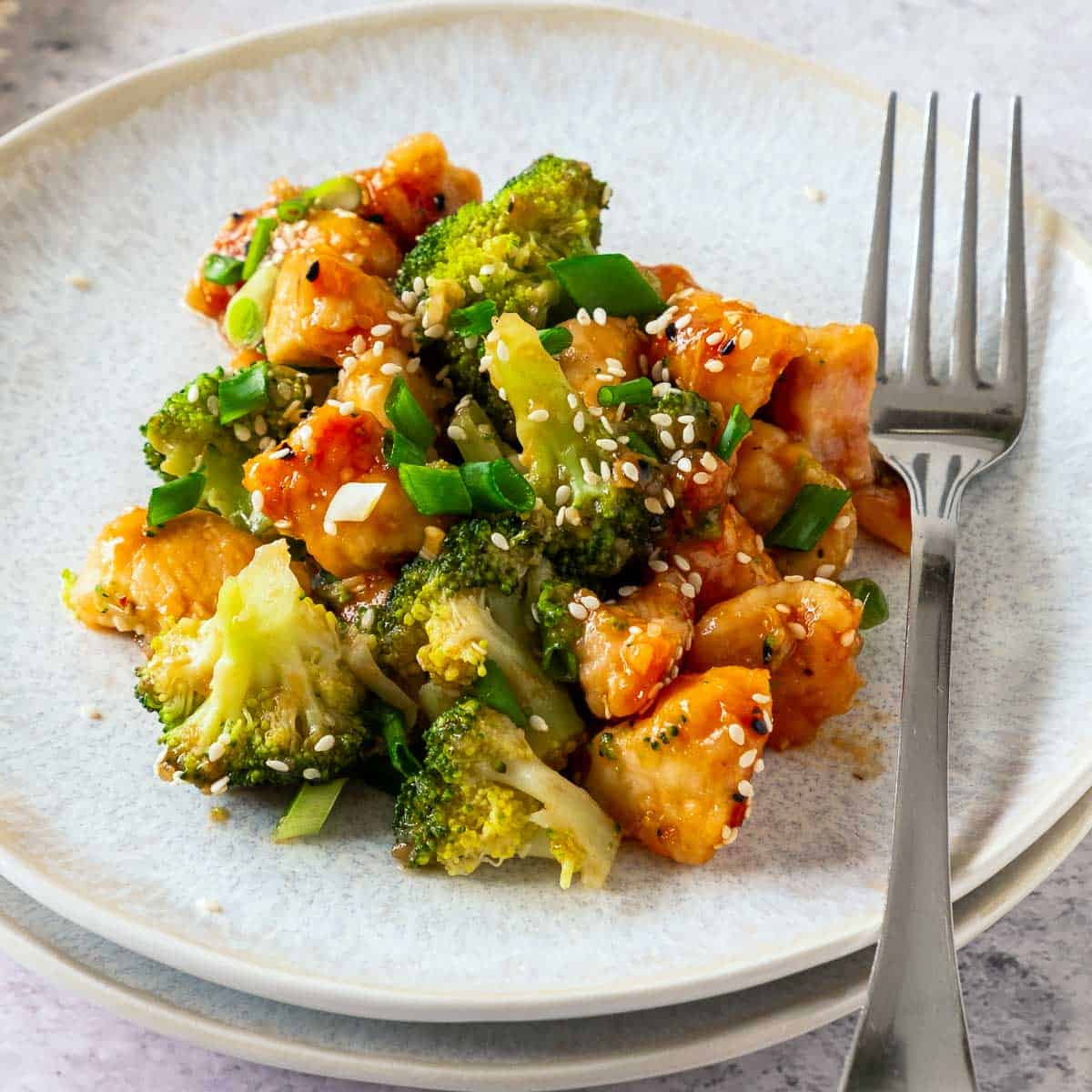 Honey garlic chicken on a white plate with fork on the side.