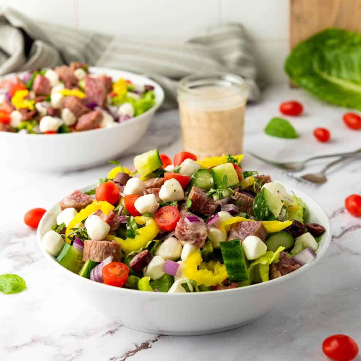 Side view of Italian chopped salad bowls placed on marble surface with dressing jar in the background. 