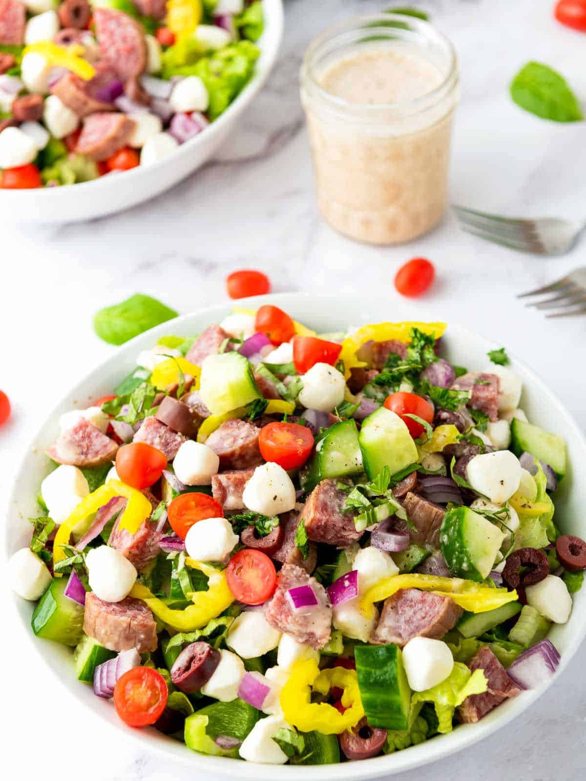 Two bowls of Italian chopped salad along with a jar of dressing in the background.