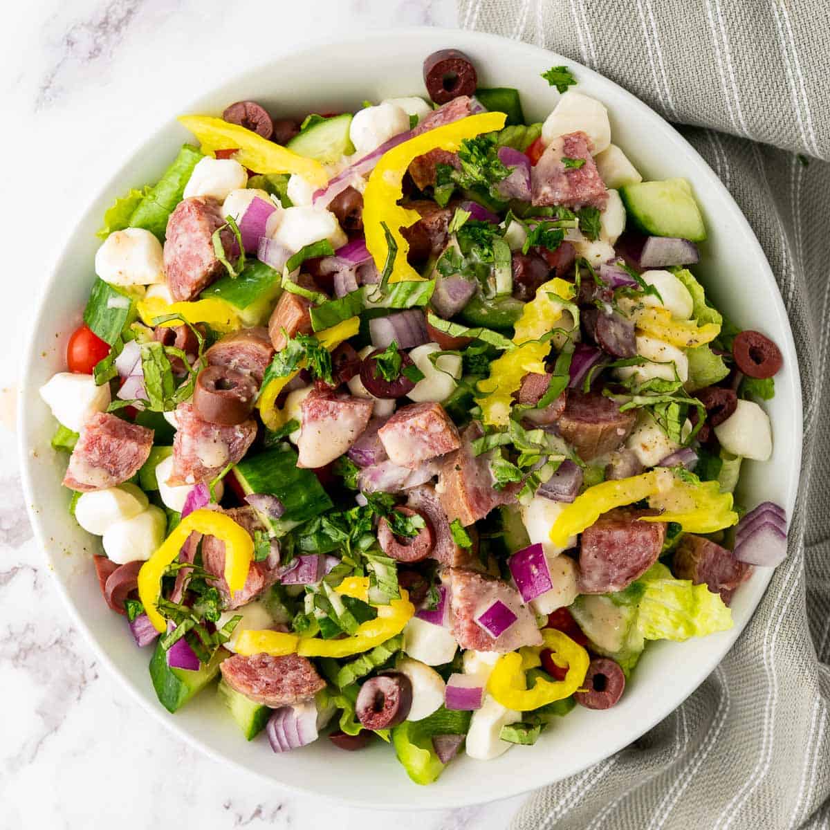 Salad ingredients tossed with dressing in a large white bowl.