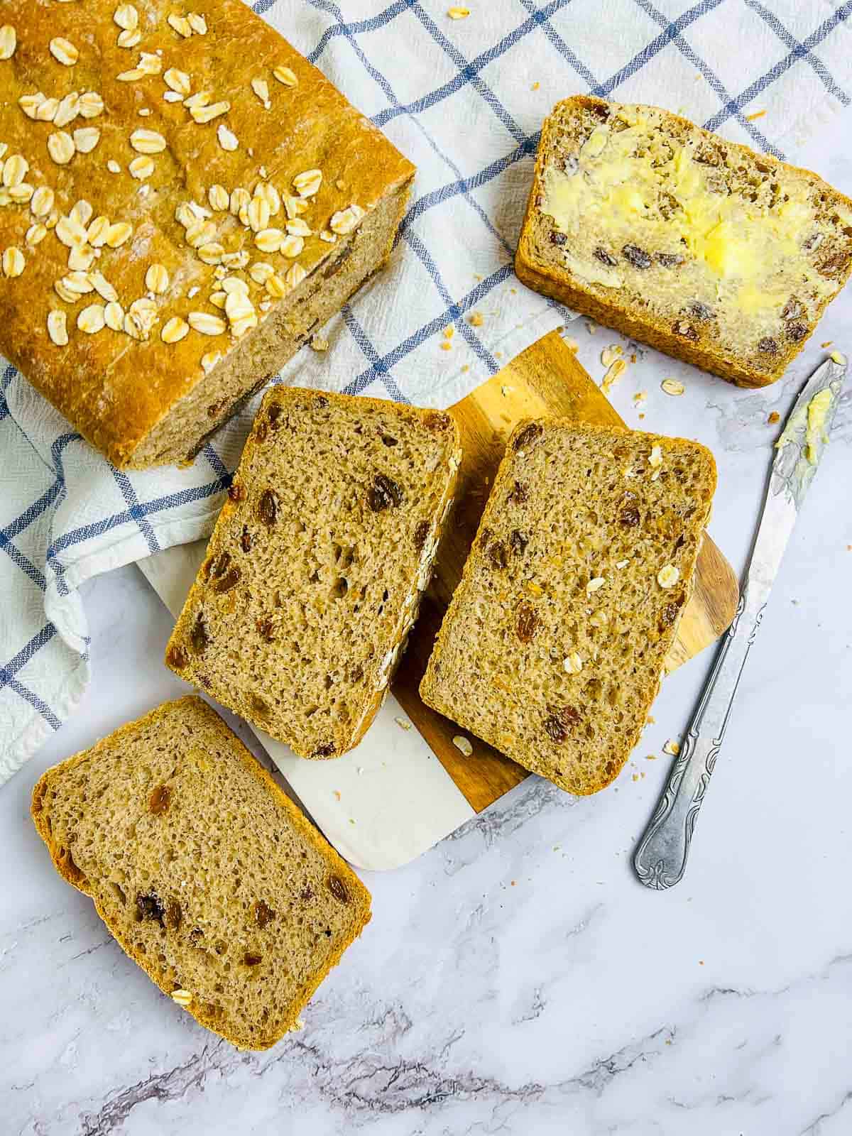 Slices of oats raisin bread with one buttered slice.