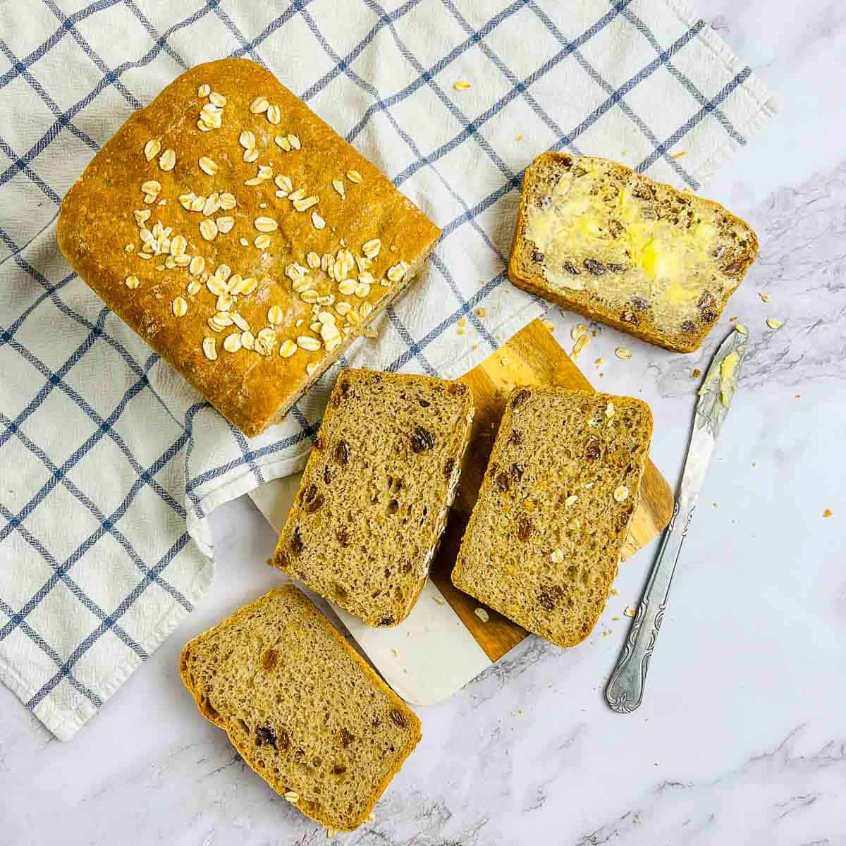 Loaf of oats raisin bread with three cut slices on a wooden board.