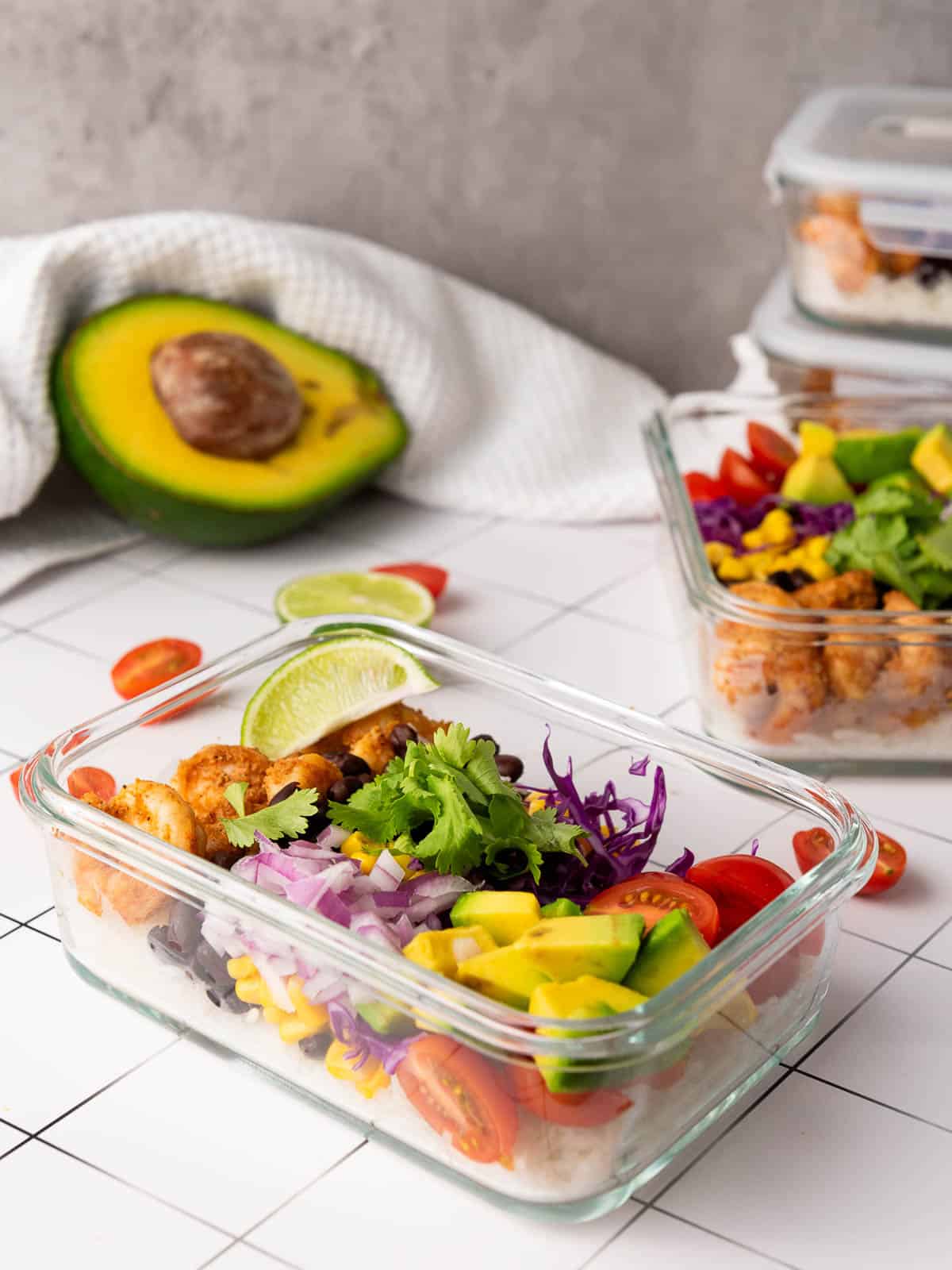 Stacked meal prep containers with avocado in the background.