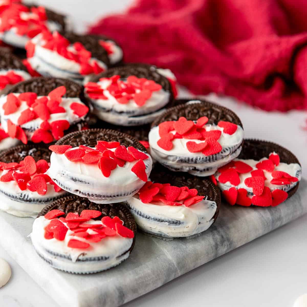 White chocolate dipped oreos on a marble board with red cloth in the background.