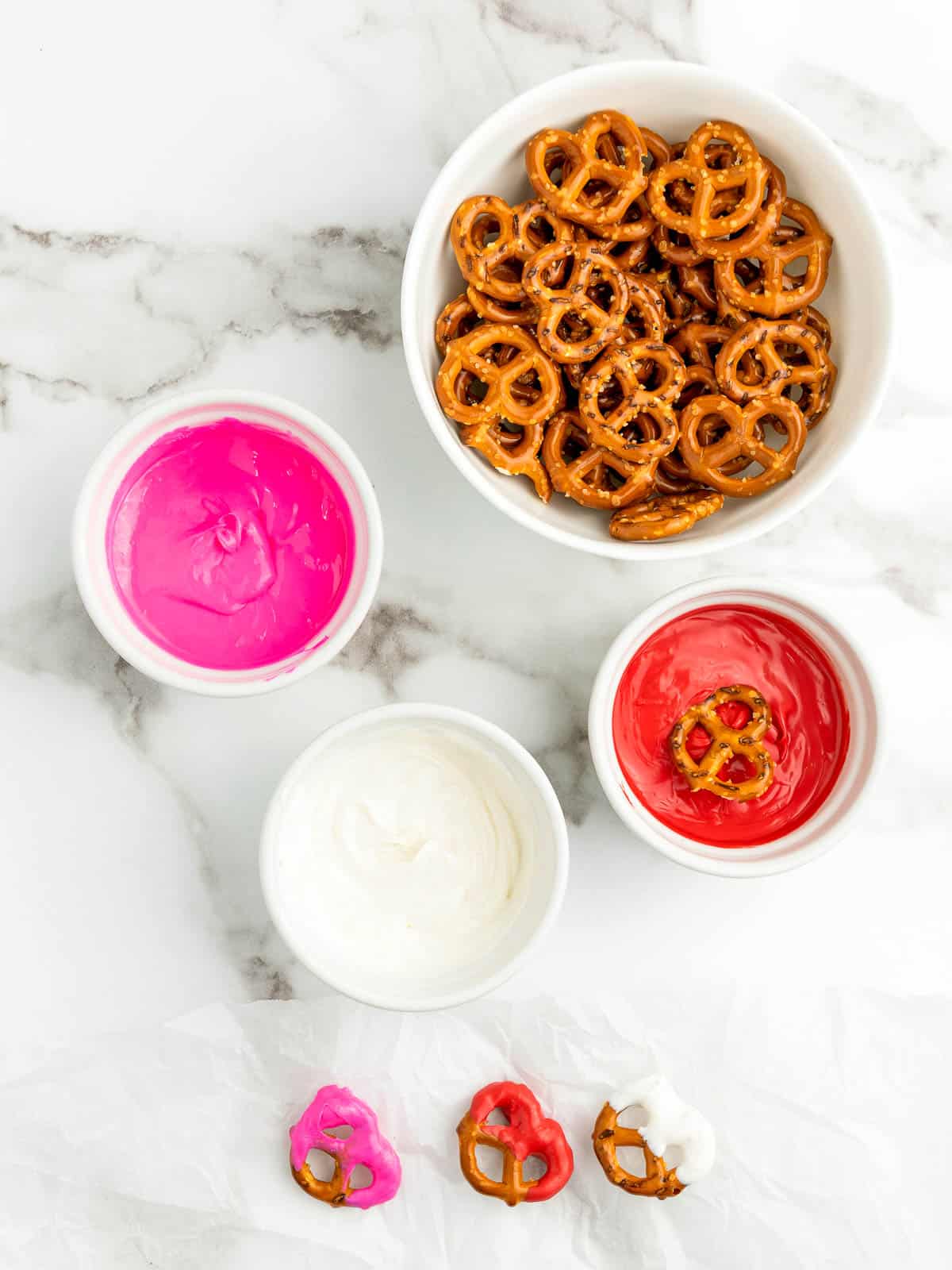 Melted candy in small bowls with some dipped pretzels.