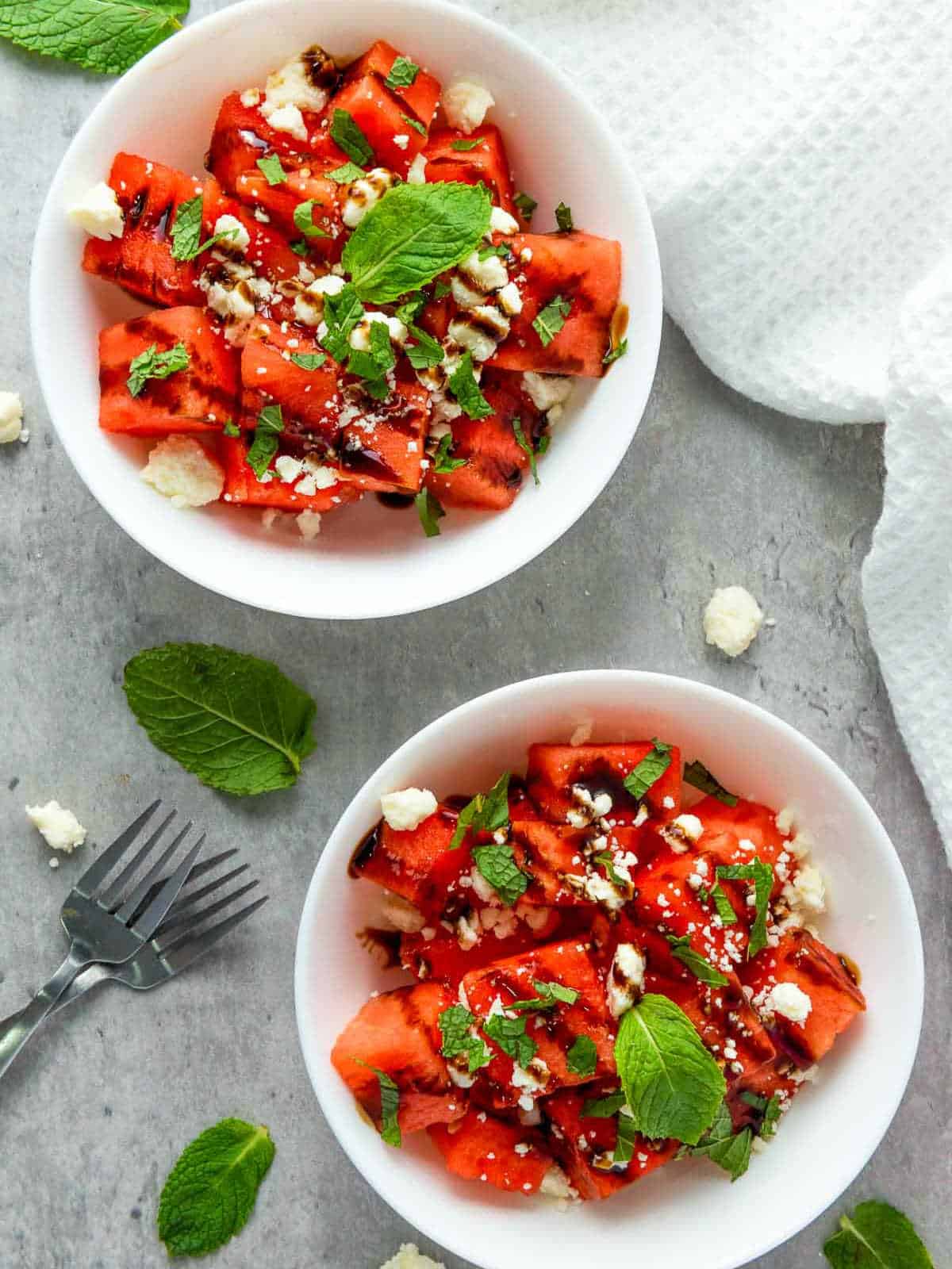 Two bowls of watermelon feta salad on a grey board.