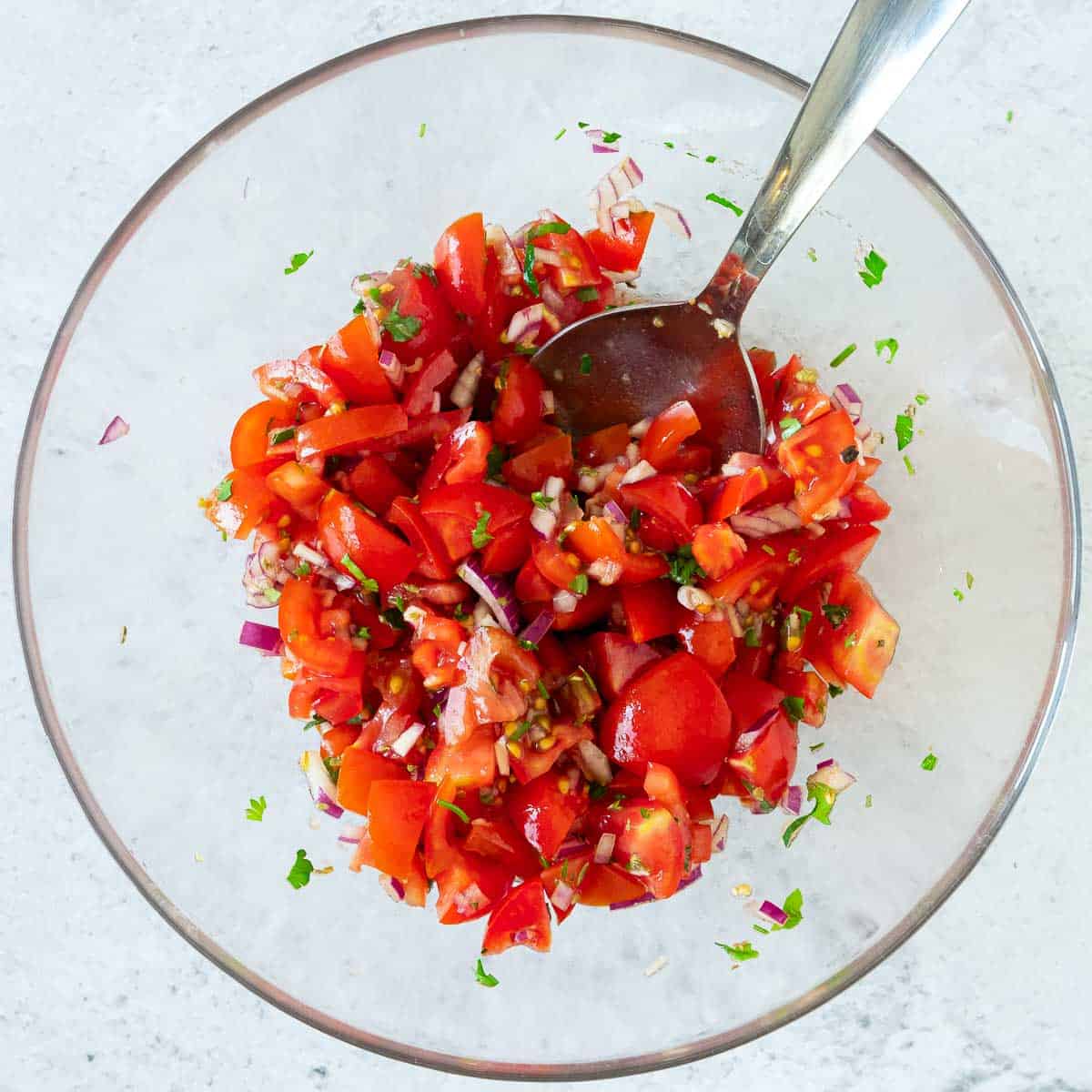 Tomatoes and other ingredients tossed in a mixing bowl.