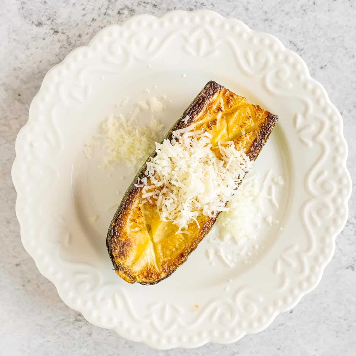 Cooked piece of zucchini placed on a serving plate and topped with grated cheese.