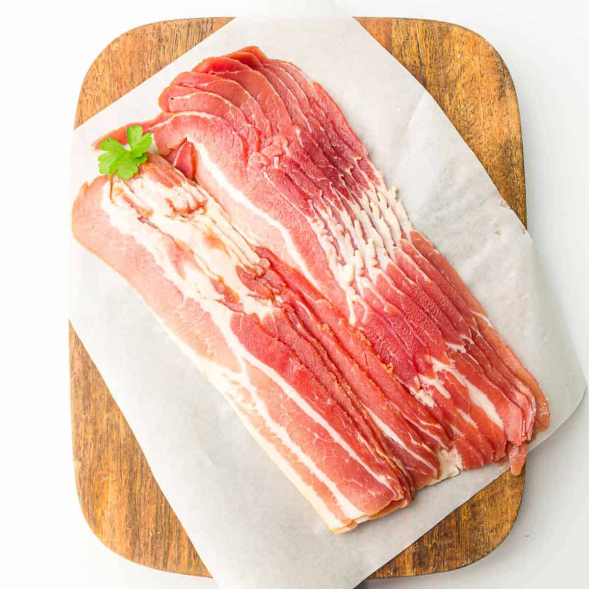 Uncooked bacon strips on a wooden board.