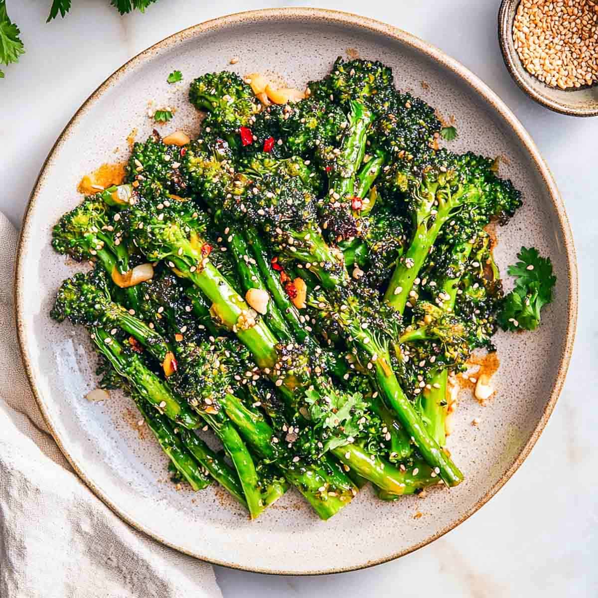 Asian-style broccolini served on a white plate with sesame seeds in the background.