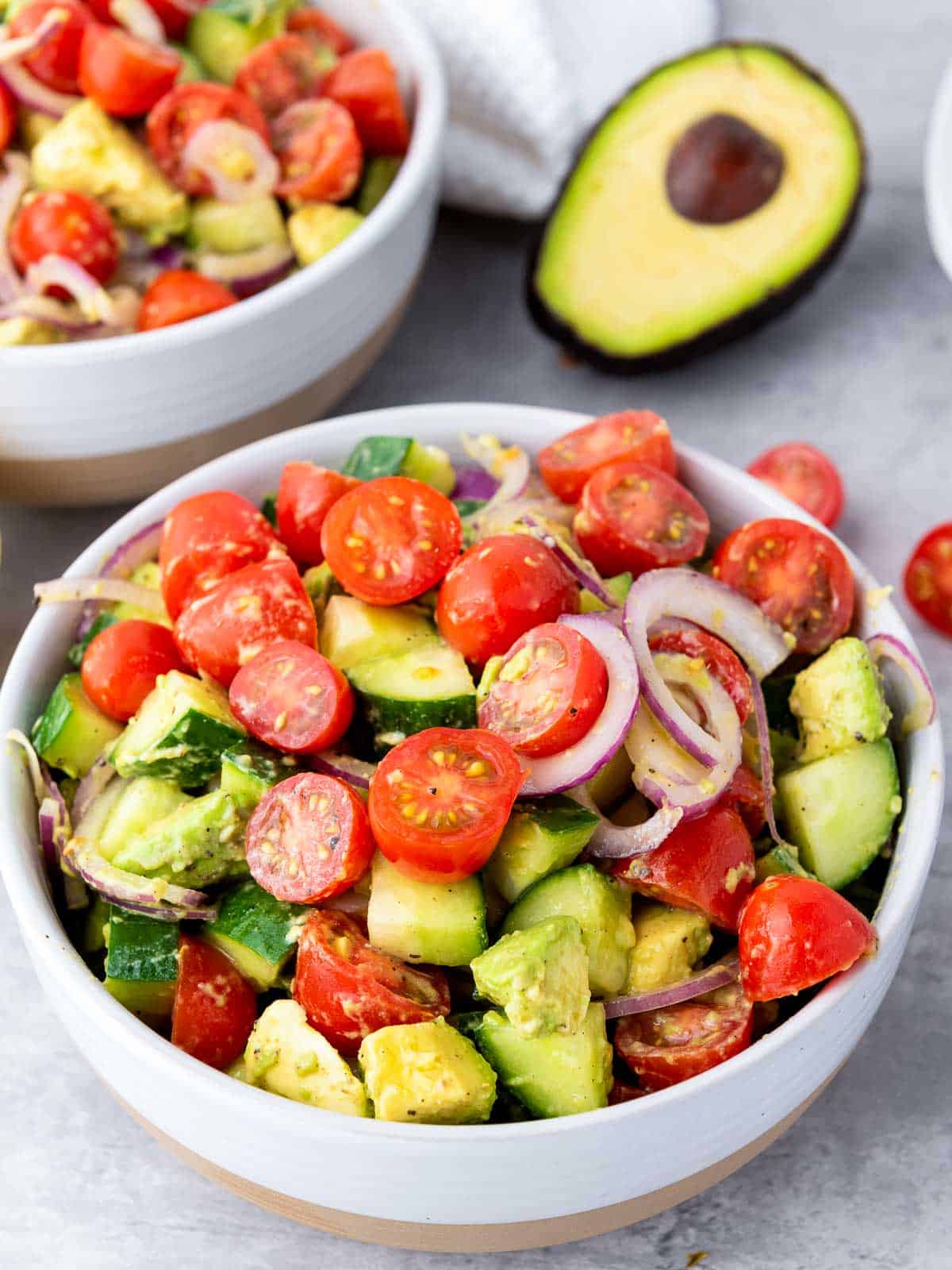 Two bowls of avocado salad on a grey surface.