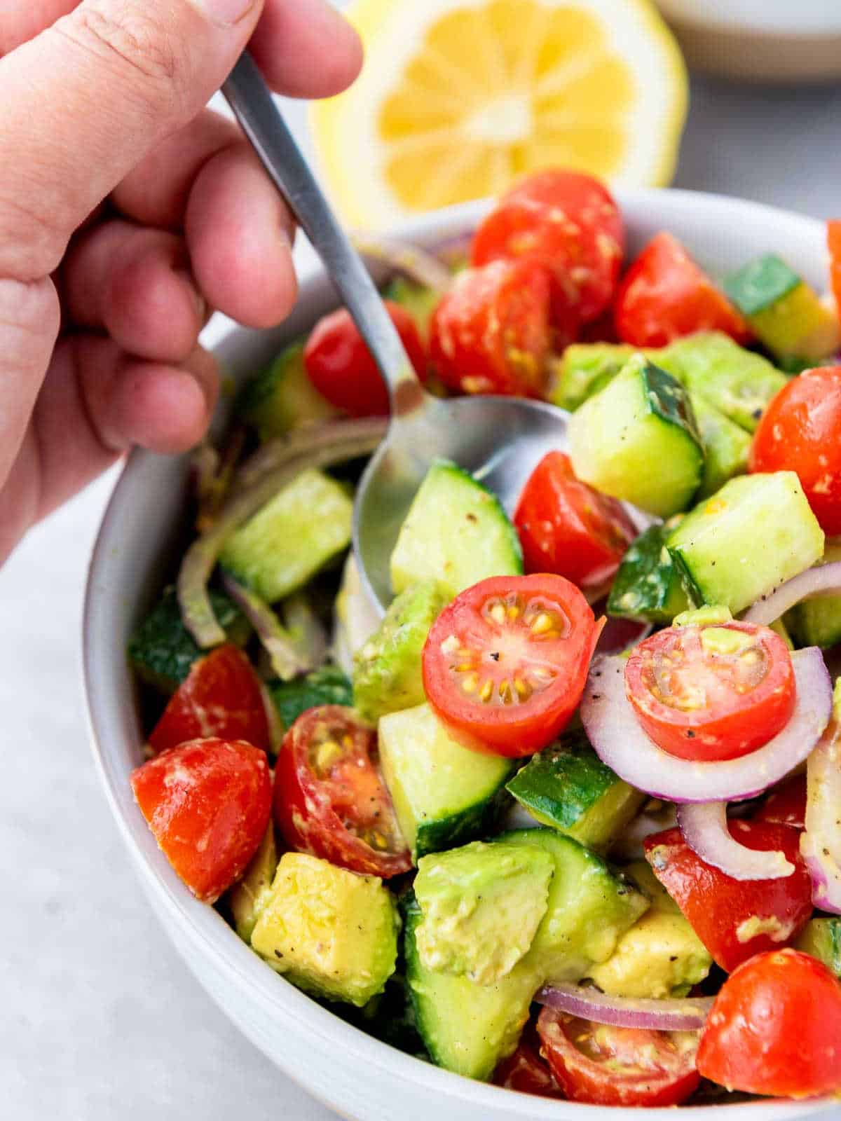 Salad vegetables on a fork over a white serving bowl.