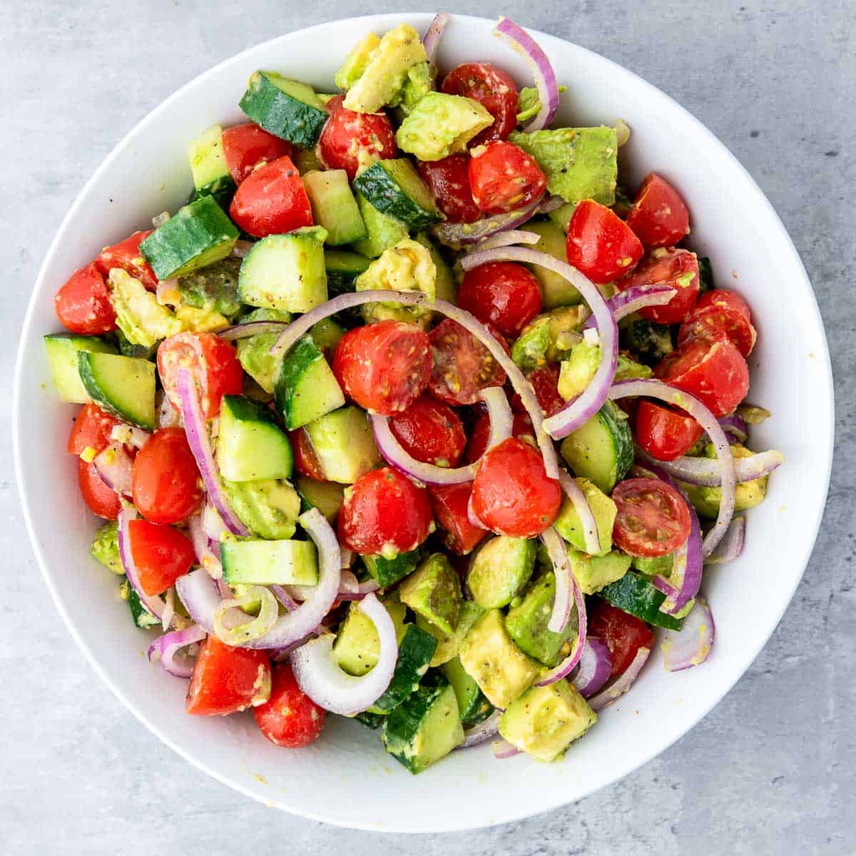 Seasoned and tossed salad in a wide mixing bowl placed on a grey surface.