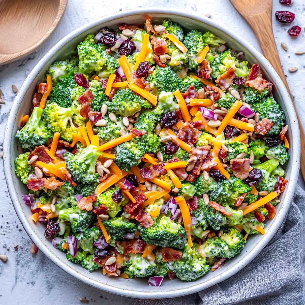 Broccoli salad placed in a wide serving bowl with wooden salad spoon in the background.