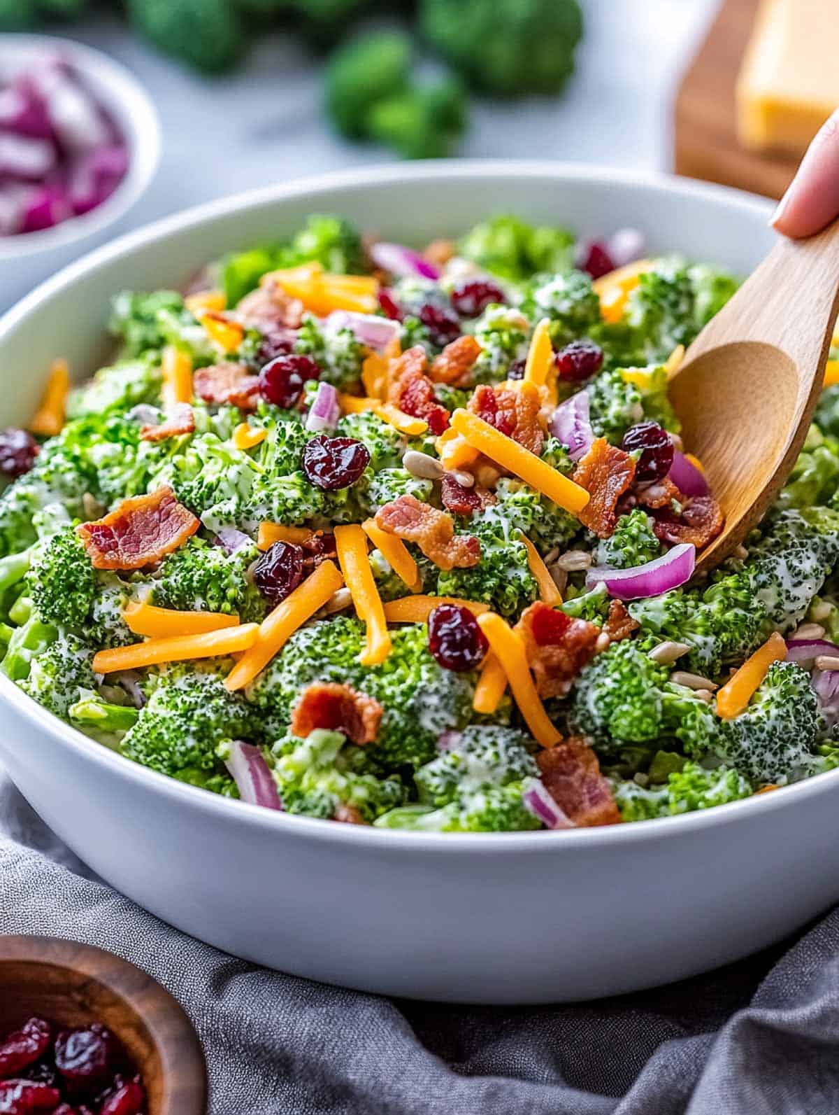 Broccoli salad being served from the bowl using a wooden serving spoon.