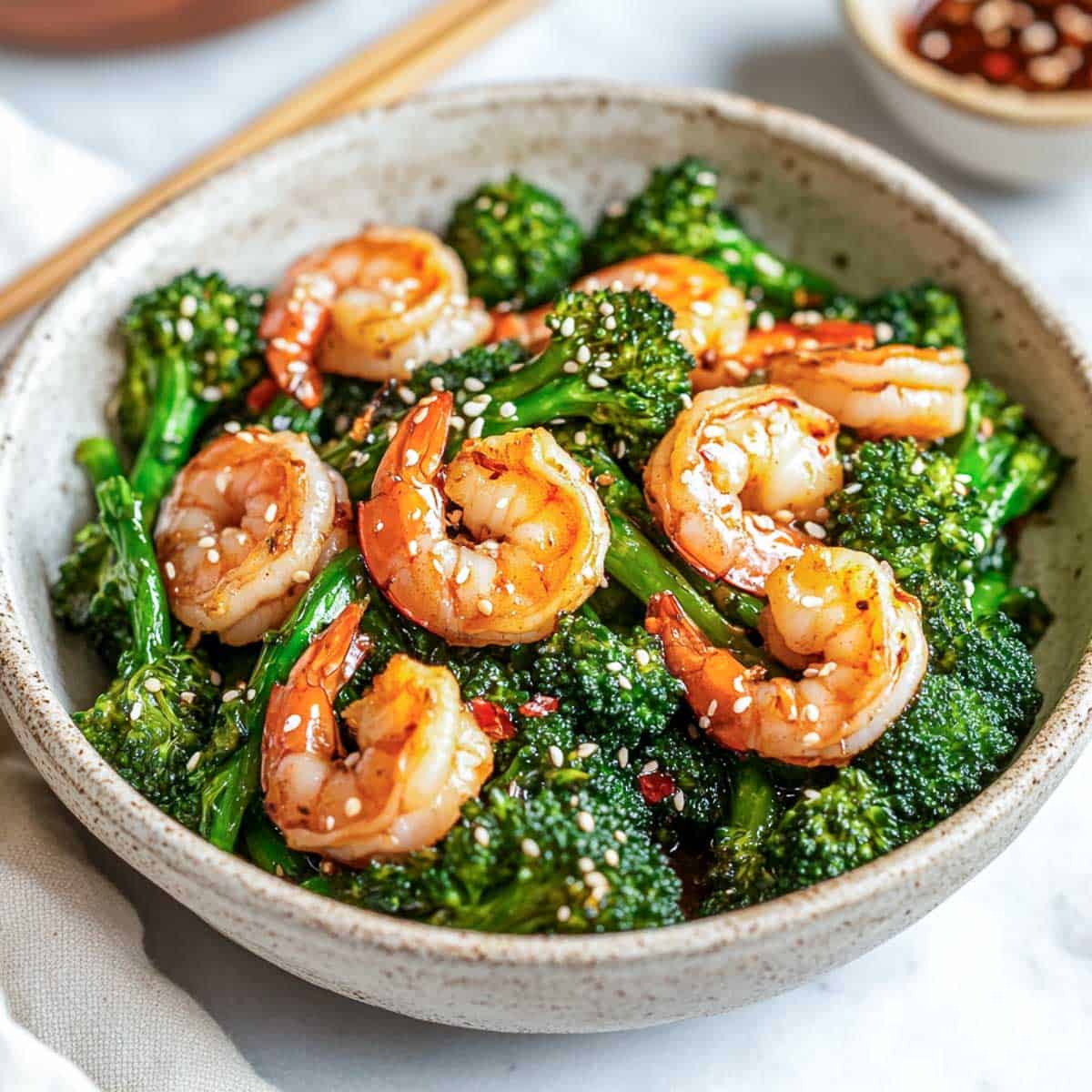 Broccolini and shrimp stir fry served in a wide bowl with chopsticks in the background.