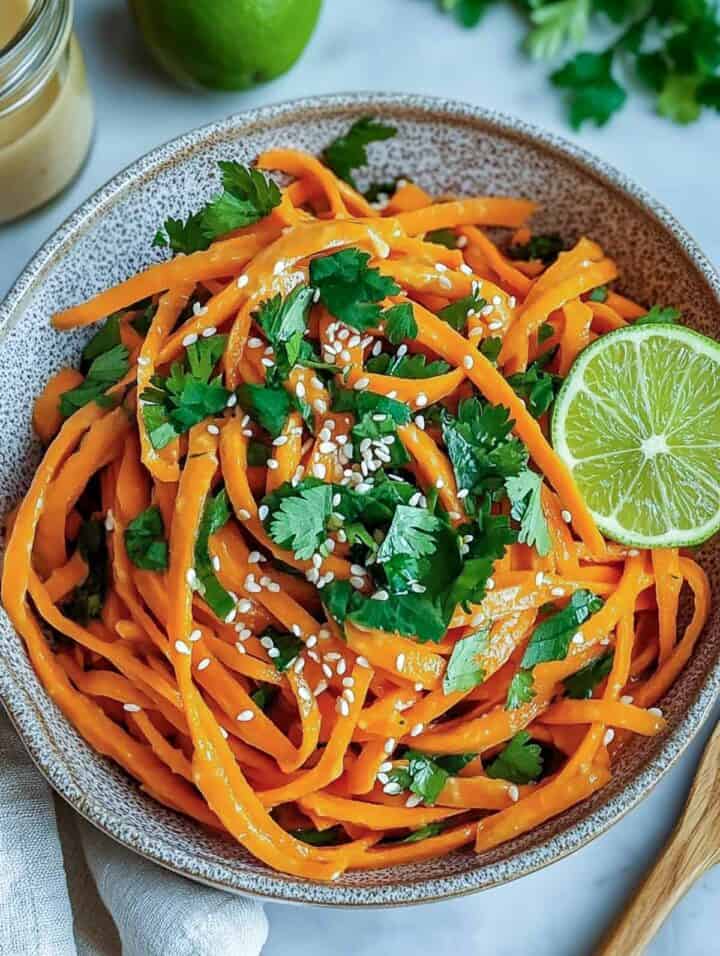 Close up of carrot salad topped with parsley and lime slice in a grey bowl.