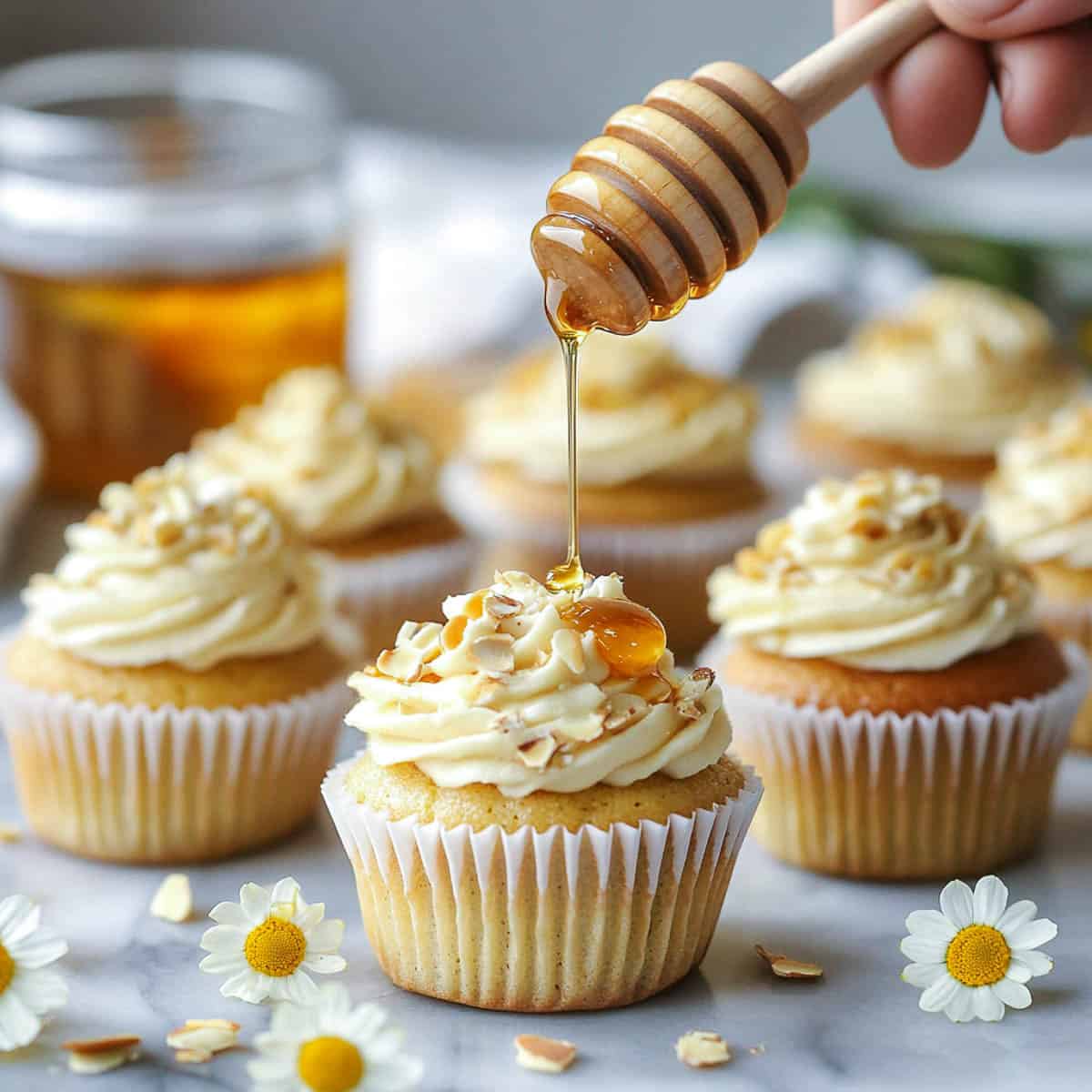 Chamomile cupcakes on a marble surface with honey being drizzled from top.