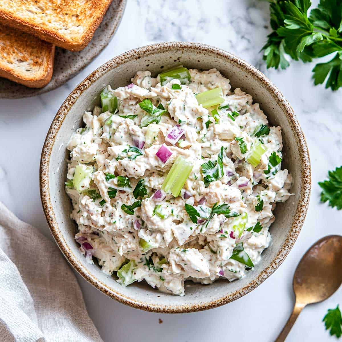 A bowl of chicken salad garnished with celery and served with toasted bread.