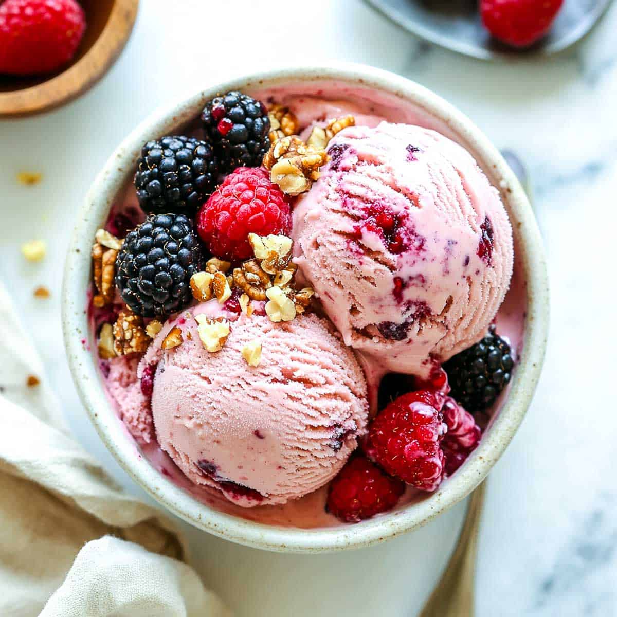 A bowl with strawberry ice cream placed on a marble surface and topped with fresh berries.