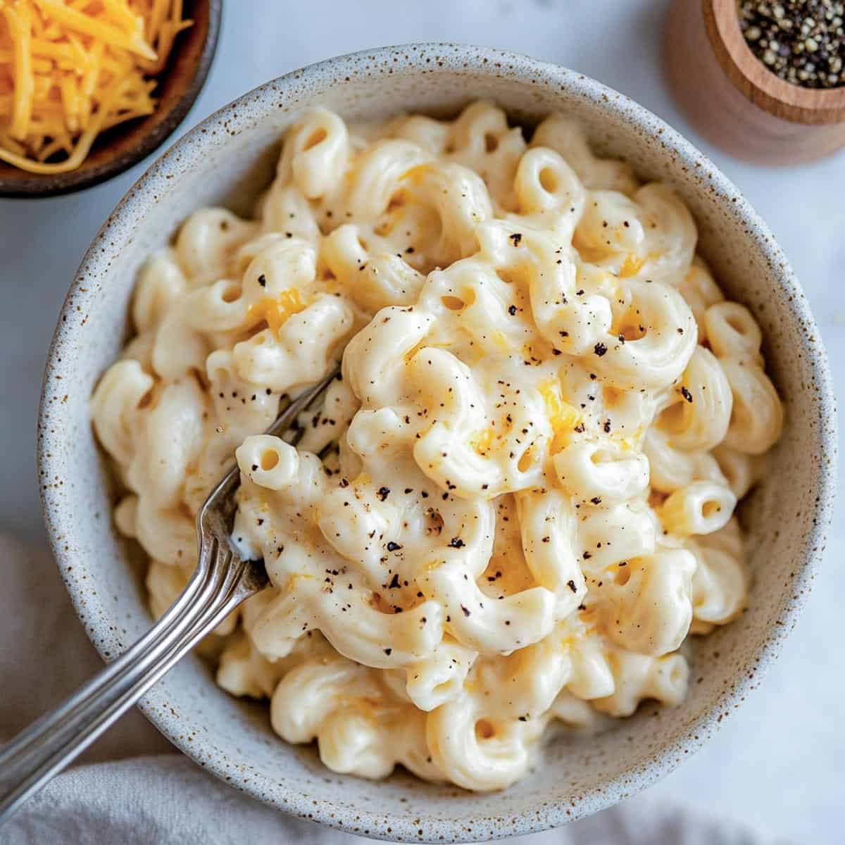 A bowl of mac and cheese on a white marble surface.