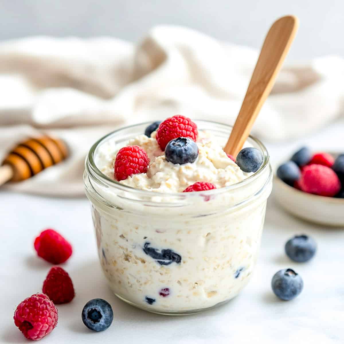 Cottage cheese overnight oats jar with berries and honey spoon in the background.