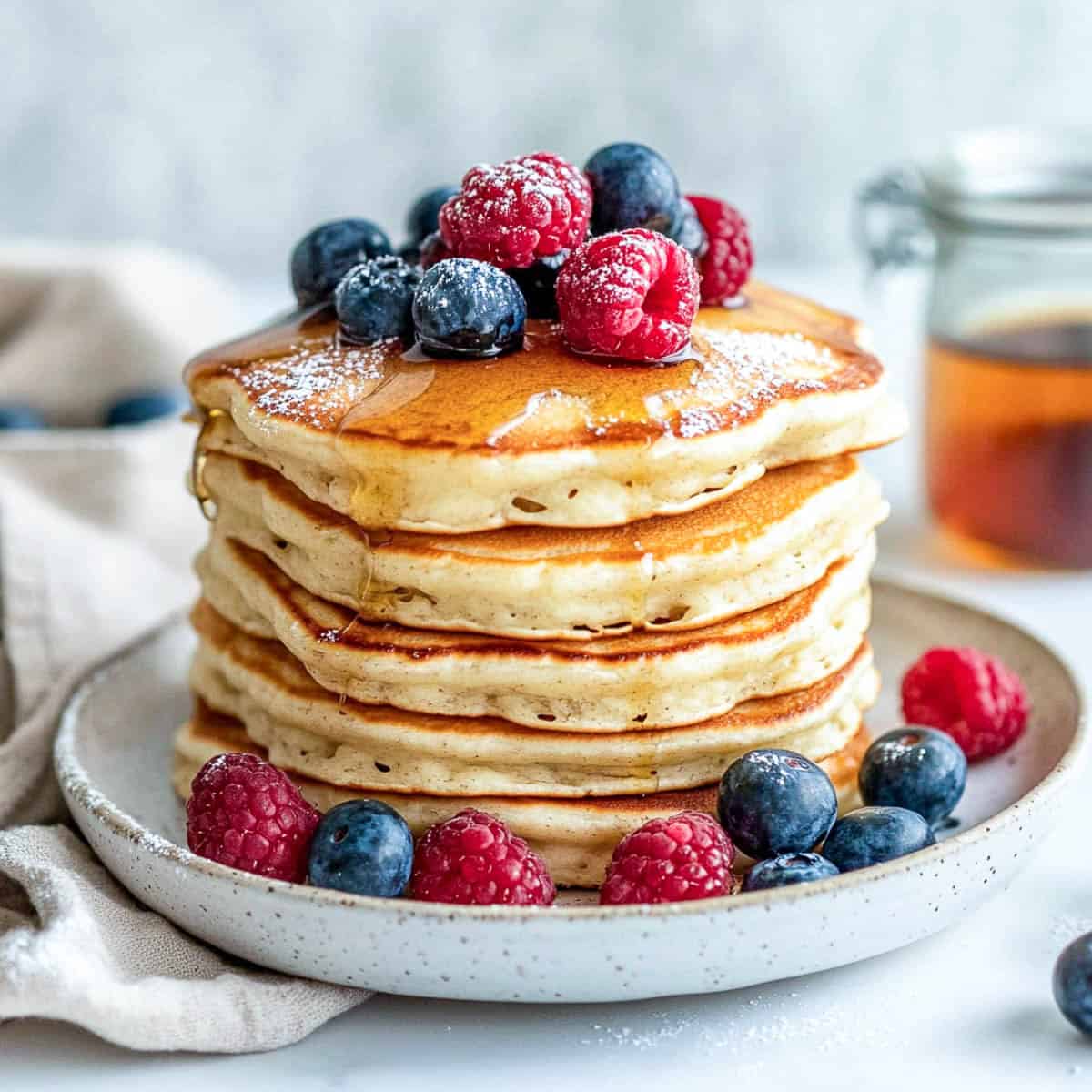 Side view of a stack of pancakes topped with berries and syrup.