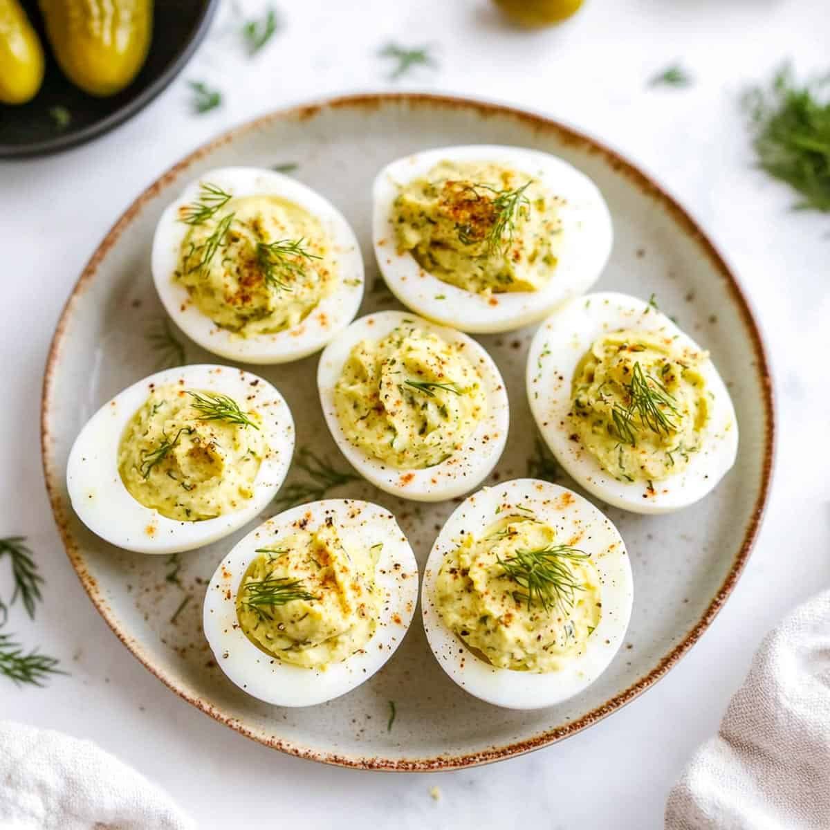 Dill pickled deviled eggs with a bowl of pickles in the background.