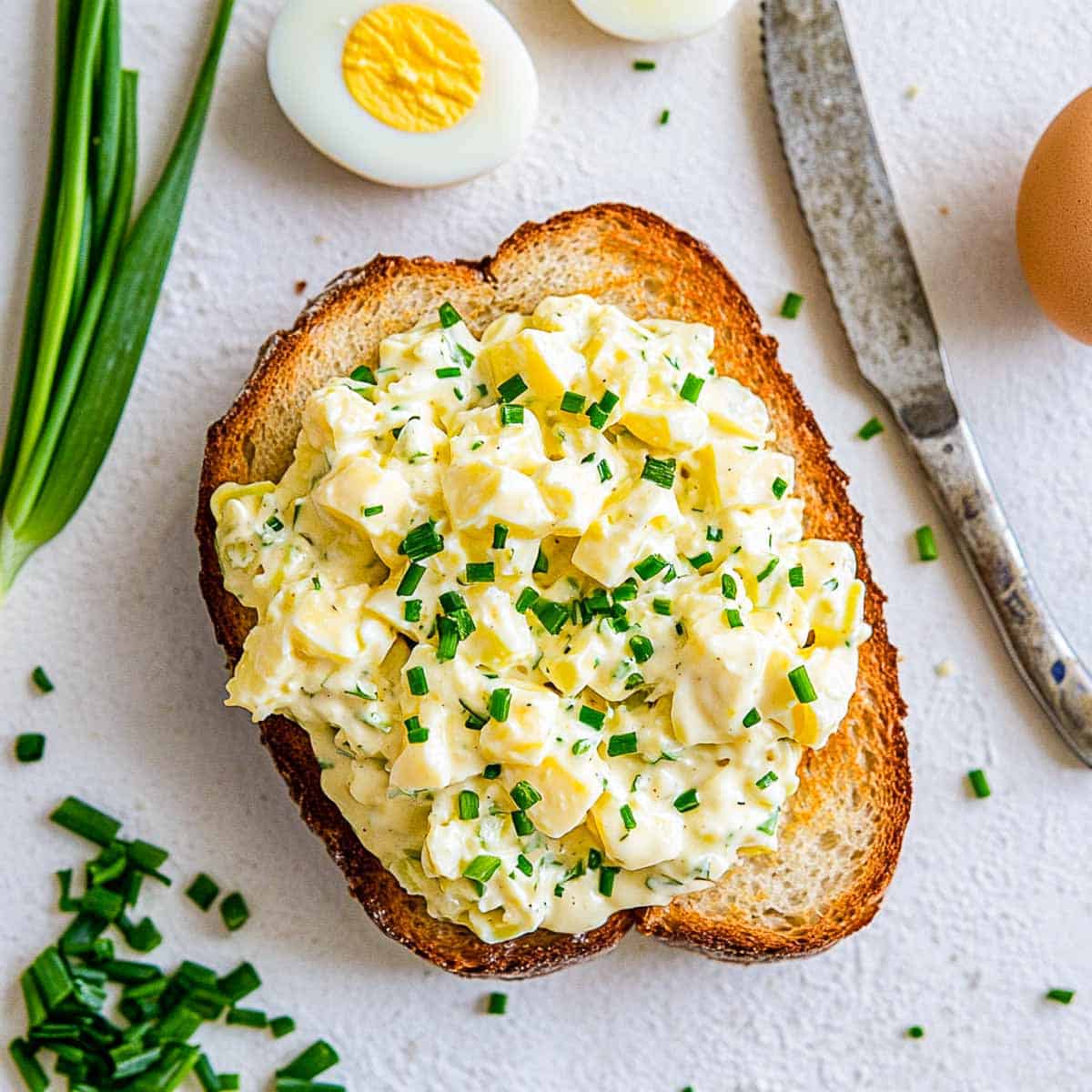 Egg salad spread on a toasted bread and placed on a white surface.