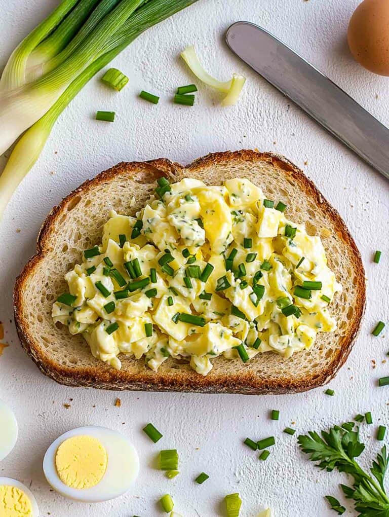 Egg salad on a white board with leek and boiled eggs in the background.