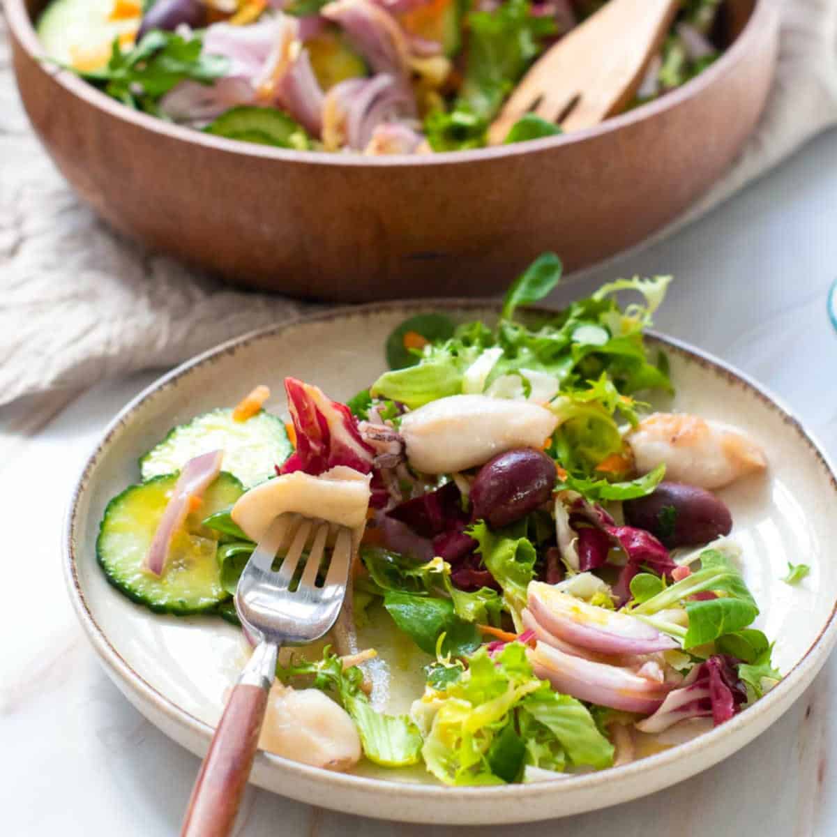 Side view of garden salad in a plate and serving bowl with a calamari on the fork.