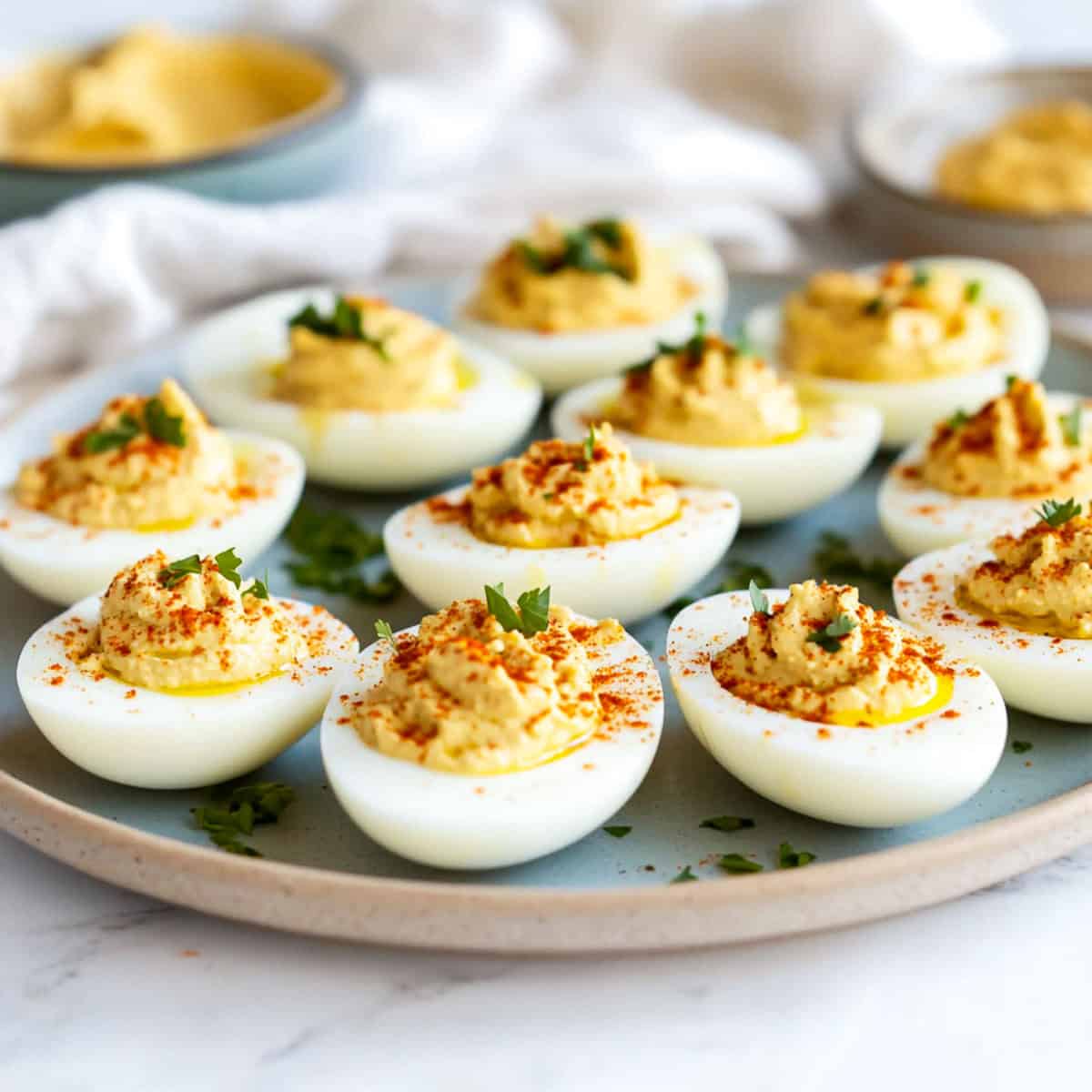 Hummus deviled eggs on a grey serving plate with a bowl of hummus in the background.