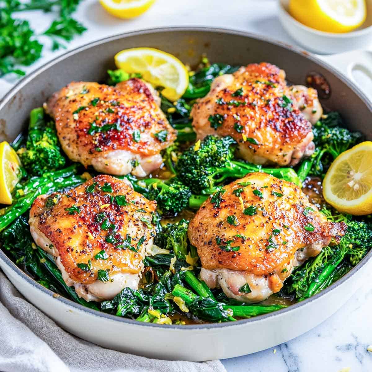 A wide serving bowl of lemon garlic chicken and broccolini garnished with fresh lemon slices.