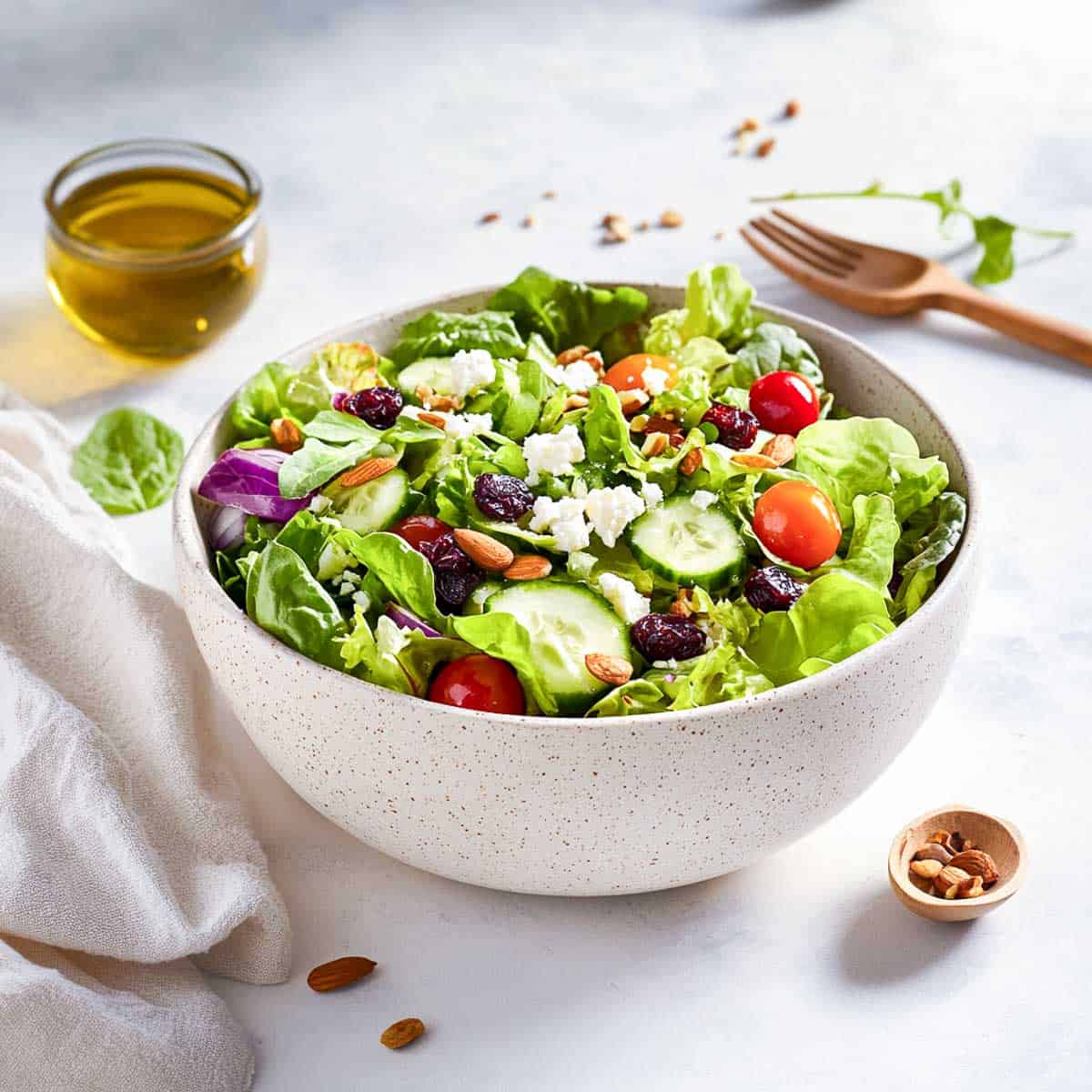 Spring mix salad in a white bowl with a bowl of olive oil and salad fork in the background.