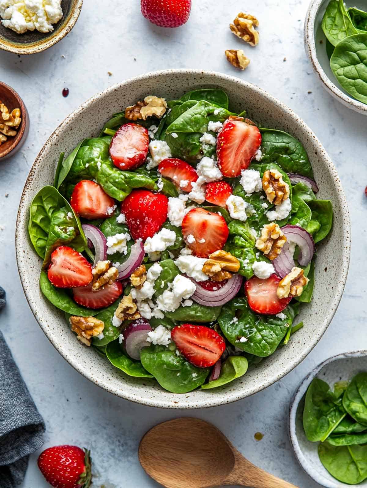 Strawberry spinach salad in a bowl placed on a grey surface with spinach and walnuts in the background.