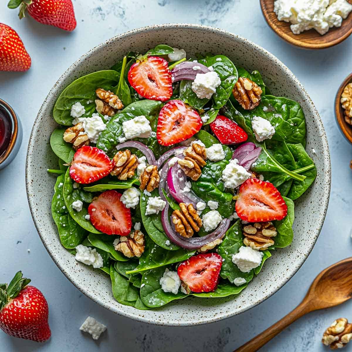 Strawberry spinach salad in a wide serving bowl with wooden handle in the background.